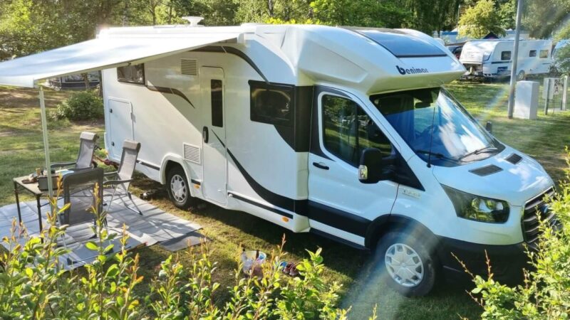 Benimar Wohnmobil mit ausgeklappter Markise und Campingstühlen auf grünem Campingplatz